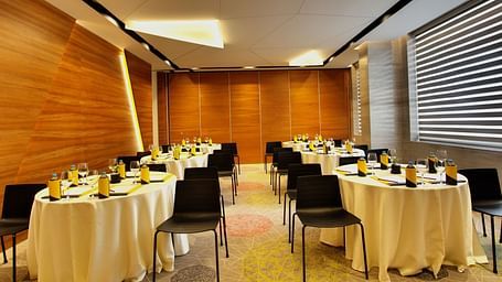 Meeting hall with round tables and chairs around with wooden wall background.