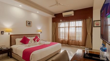 Comfortable hotel room at Diamond Palace Lords Plaza featuring a double bed with bright pink accents and a mounted television.