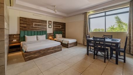 Extended view of the double and single bed, dining table and open glass windows in the Suite of Hotel Highway King in Behror.