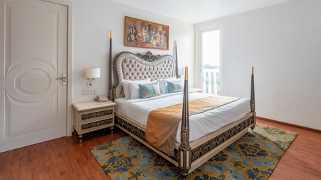 Elegant bed with a tufted headboard, ornate wooden frame, and a colourful painting above the bed at Hotel Hukam's Lalit Mahal.