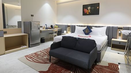 A room at Hotel Kyzen HiTech City – Your Zenly Stay with a bed, couch, desk, and mini-fridge setup.