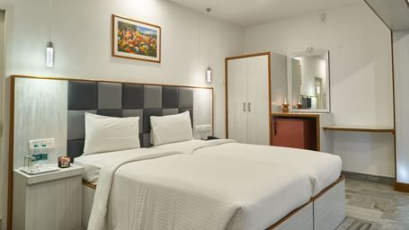 A comfortable and well-appointed hotel room at Hotel Mamallaa Heritage, featuring a large bed with crisp white linens, a bedside table, and wall-mounted art.