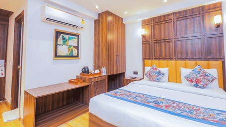 A neatly decorated hotel room with a large bed, wooden headboard, and a colourful bed runner - Hyphen Business Hotel, Noida