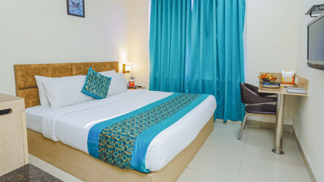 A modern hotel room with a double bed, blue curtains, a desk, and a television - Hyphen Grand, Haridwar