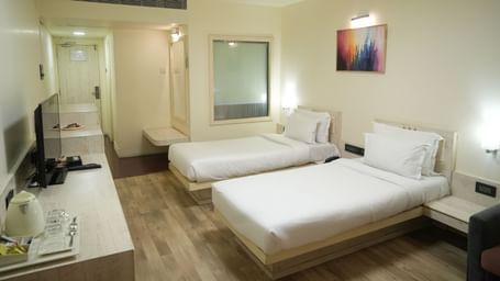 Bedroom with 2 single beds, a television, desk and wall paintings at Infiniti Hotel, Indore.