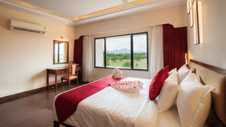 A bright, modern Presidential Suite with a king sized bed, a desk and chair by the window, and a scenic view of greenery and mountains outside