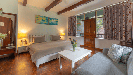 A double room layout featuring a comfortable bed, a grey couch, and floral patterned curtains - Johnson Lodge & Spa, Manali