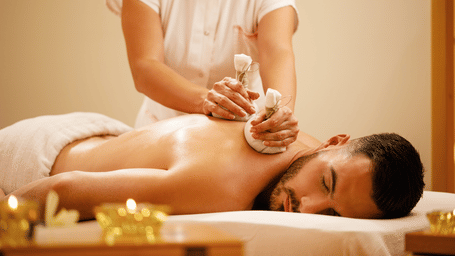 Woman using herbal pouches to massage a man's back.