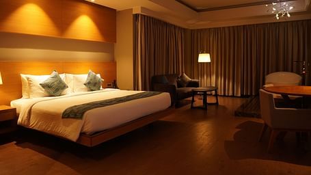 Spacious room with a large bed, cushioned furniture, and closed window curtains