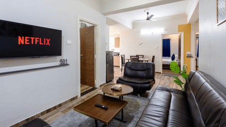 The living area in the separate living room of the 4BHK of Kove Smart Stays, seen with the multiple sofas facing the wall-mounted television.