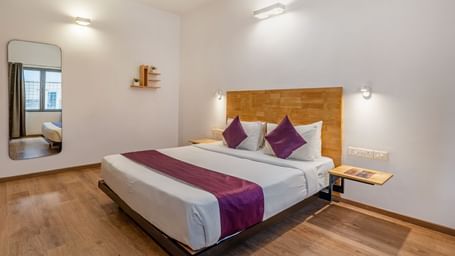 A hotel room with a double bed, wooden flooring, a large mirror and a side table - Monday Hotels HITEC City, Hyderabad
