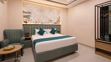 Studio Suite bedroom with a king bed, teal cushions, tropical mural, wingback armchair and open wardrobe at Monday Hotels & Suites Madhapur, Hyderabad.