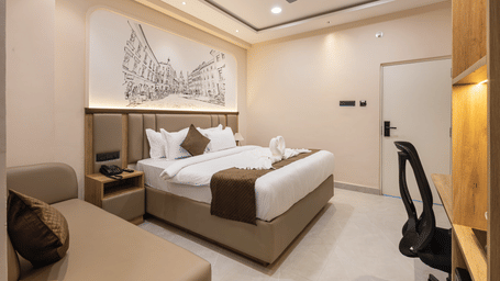 A bedroom with a king size bed, a sofa seating area, a desk with a chair, and wall art at Monday Hotels & Suites Madhapur Hyderabad.
