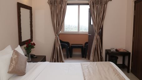 A bed facing a window with curtains, bedside tables and flowers at Nazri The Verda Hotel, Arambol.