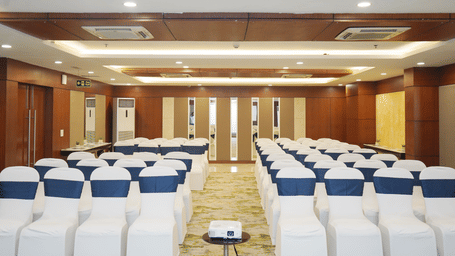 A wide view of an empty conference hall with neatly arranged theatre-style seating and rich wooden wall panels.