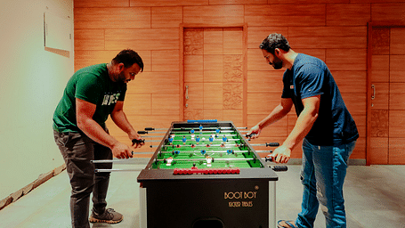 Two people playing foosball at Nirantara Resort & Spa in a room with wood-panelled walls.
