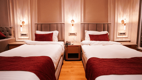 A room at Orsino Spa Resort with two single beds, each dressed in white linen with a red bed runner, and wall-mounted lights.