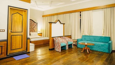 A room at Orsino Spa Resort, furnished with a bed, a small sofa, a wooden table, and a wardrobe, with light-coloured walls and curtains.