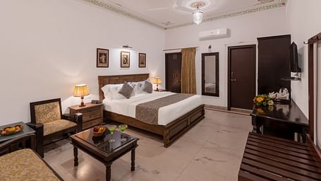 A spacious bedroom at Panna Vilas Palace, featuring a wooden table, cushioned furniture, and warm lighting | Panna Vilas Udaipur