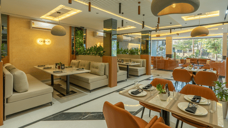 A restaurant at Perfectstayz Shree Narayana in Ujjain featuring sofa sets and chairs with dining tables which has hand towels, cutlery, and glasses.