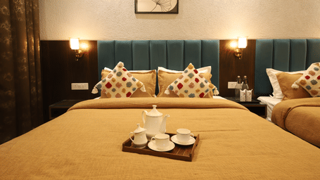 A bedroom at Perfectstayz Premium Laxmi Heritage with a king size bed, blankets, a tray with a tea set, 2 bedside tables, wall-mounted lights, and artwork in the background.