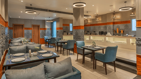 An indoor dining hall featuring set tables, chairs, and a long buffet counter at Perfectstayz Premium Mahadev Regency, Katra.
