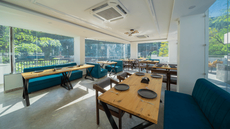 An indoor dining area with tables, benches, chairs, plates set on the tables, and a window view of trees outside in Perfectstayz Premium Mystic Falls, Rishikesh.