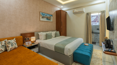 A bedroom at Perfectstayz Premium Shree Narayana, Ujjain featuring a queen bed, a yellow side chair, and a simple wooden wardrobe in the corner.