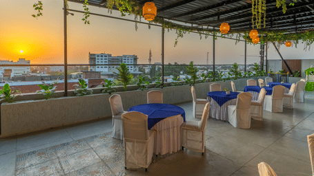 The open-air dining space at Perfectstayz Premium Shree Narayana, Ujjain offering a scenic view of the city skyline during a golden sunset.