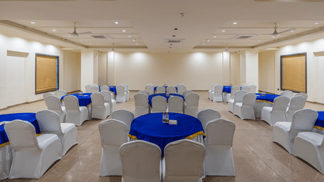 A banquet hall with multiple round tables, covered chairs, and lighting fixtures arranged for events at Perfectstayz Premium Udaipur By The Lake.