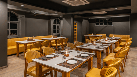 A restaurant with tables set with plates, chairs, and lighting fixtures arranged indoors at Perfectstayz Premium Udaipur By The Lake.
