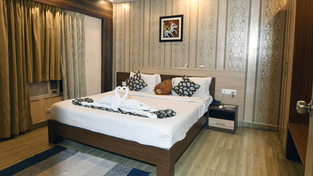 A room with a kind size bed with wooden panelling behind it featuring swan towel decoration, curtains, and a wall art at Pipul Hotel And Resort, Puri.