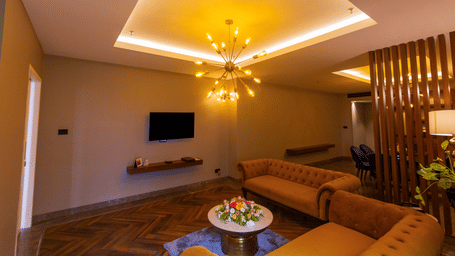 Polo Suite lounge with two tan tufted sofas, sputnik chandelier, mounted TV and wood-slat partition at Polo Hotel, Agartala.