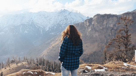 A woman standing on top of a mountain and looking at the view.