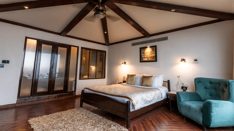 Misty Mountain Villa living area at Polo Resort Cherrapunji with cream sofas, dining table, wooden blinds, exposed beams and shag rug.