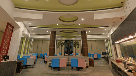 A modern dining hall features a high ceiling, colourful pink and blue chairs, and a long buffet counter at Ramada by Wyndham Bodh Gaya Mahabodhi.