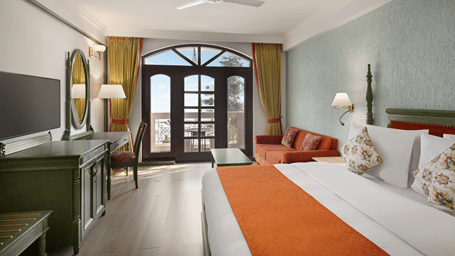 A room with a queen bed, an orange runner, a vanity mirror, and arched glass doors at Ramada by Wyndham Mussoorie Mall Road.