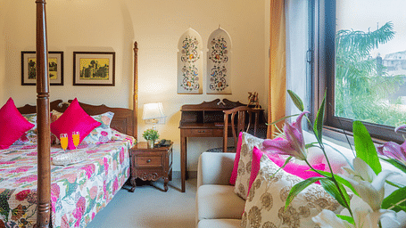 A room at Dera Rawatsar with a double bed, a work desk and chair and a sofa placed in front a window