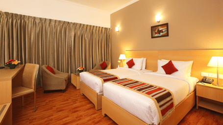 A Premium Room at Starlit Suites, Kochi, featuring twin beds, a desk, an armchair, and warm lighting.