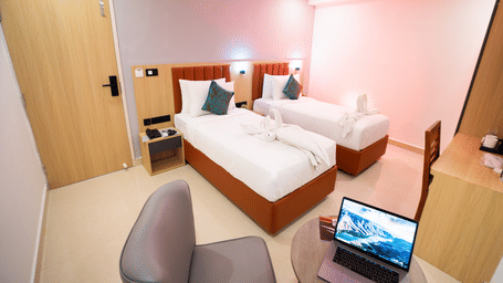 View of a room with twin beds and a laptop on a small round table with chairs on either side at Sunrise Business Hotel, Hyderabad.
