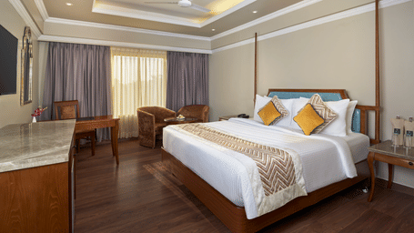 The Premium King Room at Swosti Premium, Bhubaneswar, featuring a double bed, bedspreads, pillows, chairs, tables, and a television.