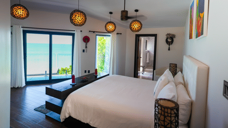 Bright bedroom with king bed, colorful wall art, and glass doors to balcony at Tamarind Hills Resort and Villas - Antigua.