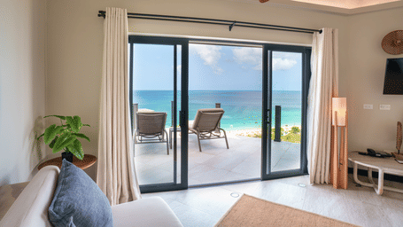 A living area with a sofa, floor lamp, ceiling fan, and large glass doors opening towards the terrace and sea in Suite 35 at Tamarind Hills Resort and Villas.