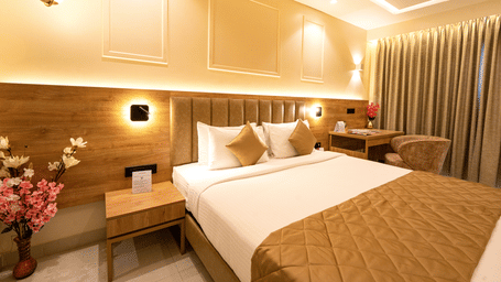 Well lit bedroom with a king bed, side table, flower vase with pink flowers and curtained windows at TGI Star Holiday Resort.