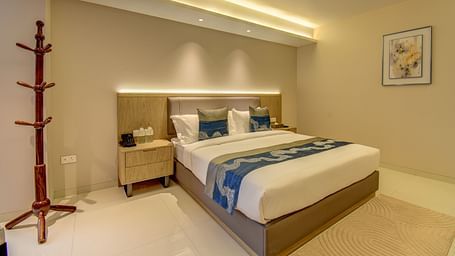 Side shot of a  well-lit Deluxe King room at The SSK Solitaire Boutique Hotel & Spa, Gangapur Road - Nashik featuring a king size  bed, two armchairs, a small table, and a work desk with a chair.