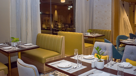 A restaurant interior with booth seating, set tables, sheer curtains, and hanging pendant lights - Urban Suites by BluSalzz, Jaipur