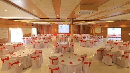 A large banquet hall in cluster seating arrangement with round tables, ready for an event at Vishal Lords Inn Gir Forest