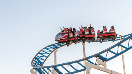 A group of people sitting inside the cars of a roller coaster ride, with their hands waving in the air/