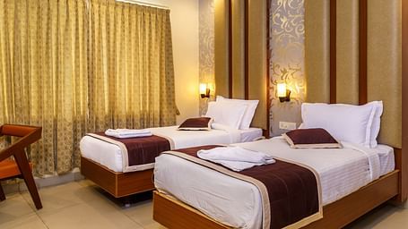 A bedroom at Wyt Hotels, Rameswaram featuring twin beds, a chair, and bedside tables with lamps for both beds.