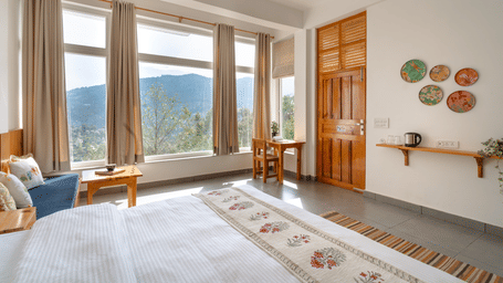 A bedroom at Ziran Retreat with a bed, a small sitting area, and large windows with a scenic view.